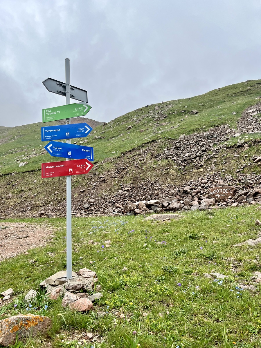Signage Post of Peaks ahead pointing to Peak Kid, Titov Pass, Medeu, and Tuyuksu T1 